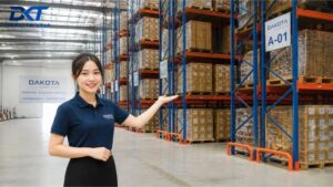 Một hệ thống kệ kho hàng công nghiệp hạng nặng với các cột trụ bằng thép màu xanh dương và các thanh xà ngang màu cam chắc chắn. Trên các tầng kệ có đặt nhiều pallet chứa thùng carton hàng hóa được xếp gọn gàng trong một nhà kho rộng lớn, lối đi rộng rãi.